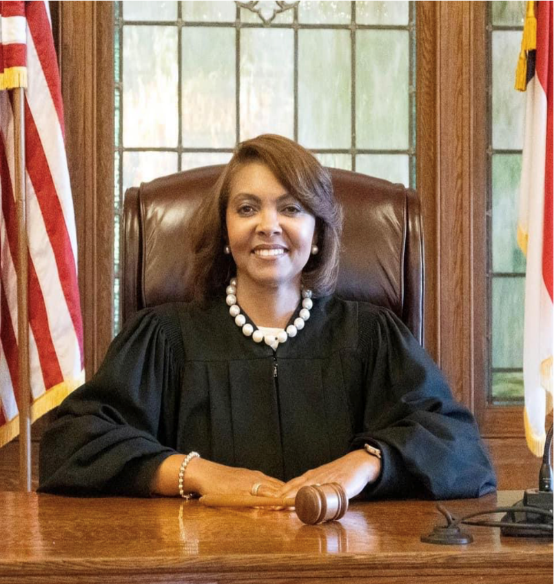 A female judge seated at her bench with a gavel in hand.