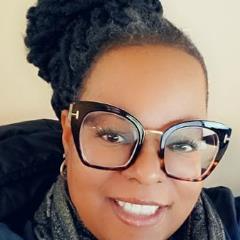 A smiling woman wearing large tortoiseshell glasses and a dark scarf.