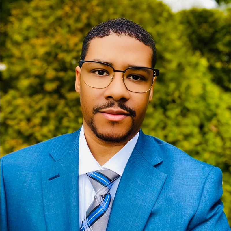 Man wearing glasses and a blue suit outdoors.