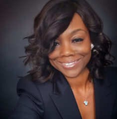 Smiling woman with wavy hair wearing a dark blazer.