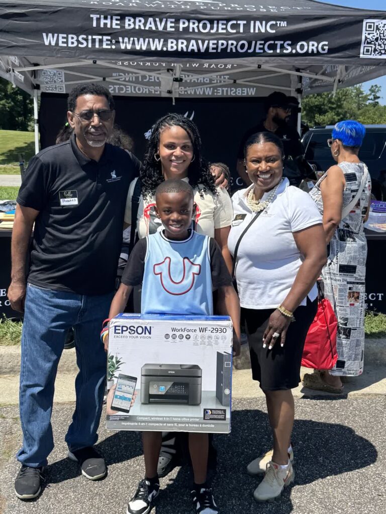 Three people smiling and holding a boxed Epson printer outdoors.