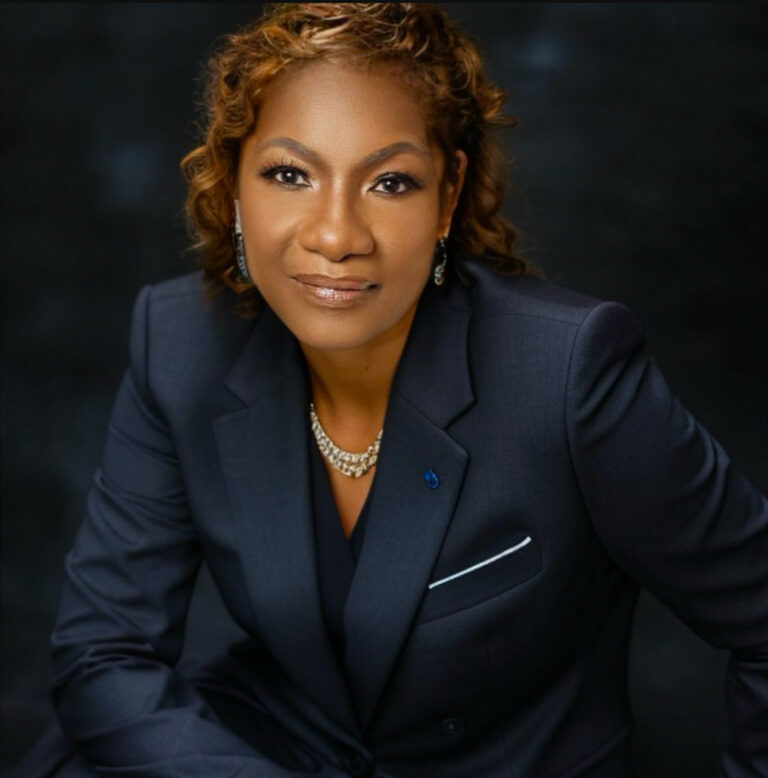 Professional woman in navy suit posing confidently against dark background.
